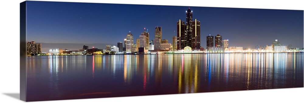 Wide angle photograph of the distant Detroit skyline, lit at night and reflecting in the waters of the Detroit River.