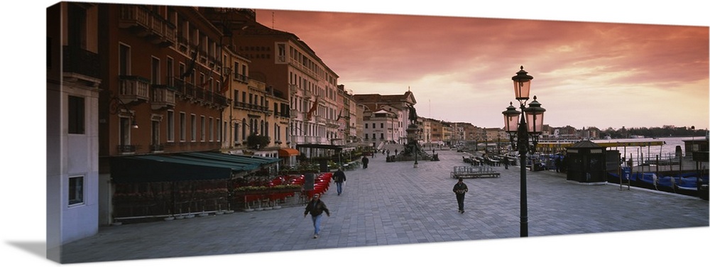 Panoramic photo of people walking on the promenade along the waterfront at sunrise in Venice, Italy.