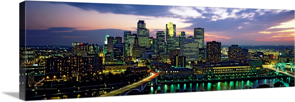 Wide angle panoramic photograph of Minneapolis skyscrapers at night, beneath a colorful sunset.