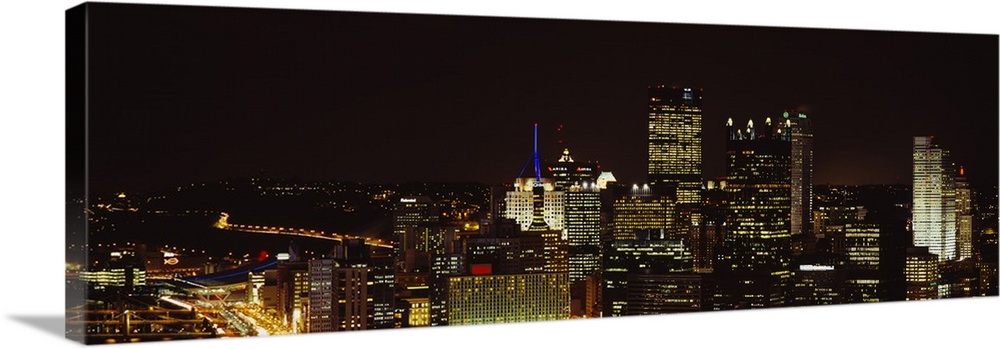 Horizontal, big, high angle photograph of the Pittsburgh skyline, with brightly lit buildings at night.