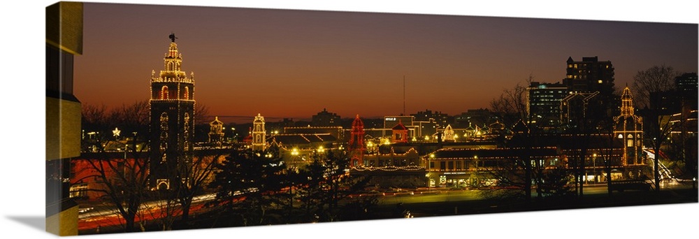 A panoramic picture of a city skyline with lights outlining the buildings and bare trees in the foreground.