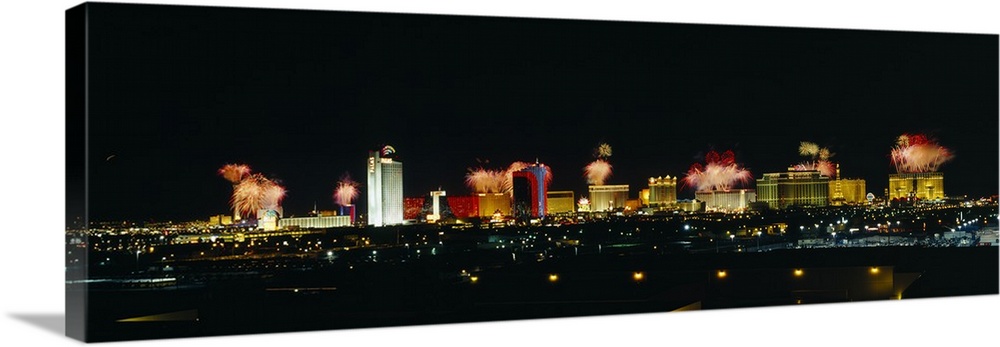 A wide angle photograph taken of the Las Vegas strip at night with the buildings lit up and fireworks exploding in the sky.