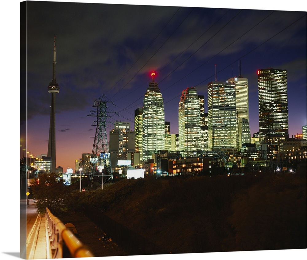 Landscape photograph taken from a street of brightly lit skyscrapers beneath a cloudy sky at night, in Toronto, Ontario, C...