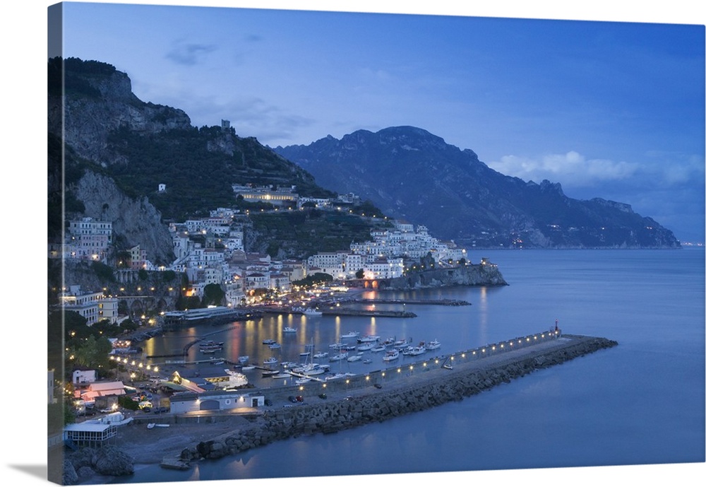 Big, landscape photograph of lit buildings along a hillside on the Amalfi Coast, in Campania, Italy, at dusk.