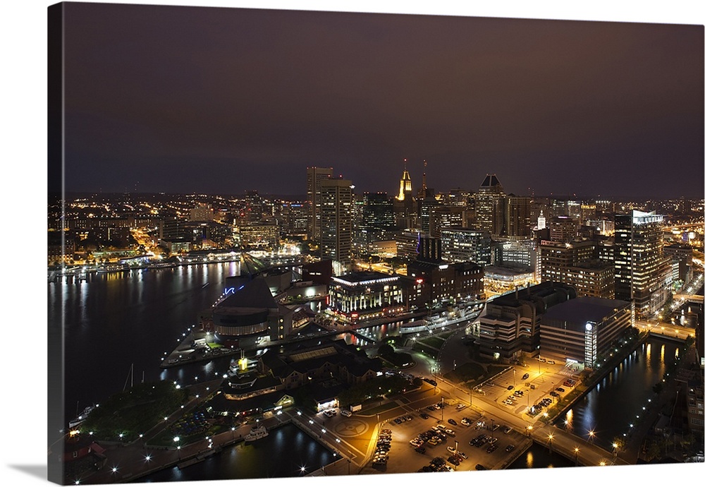 An aerial photograph taken of Baltimore during the night. Buildings are illuminated along with the edge of the harbor.