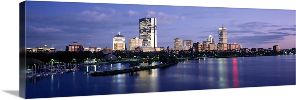 This panoramic photograph is taken at sun down of the Boston skyline with a body of water shown in front of the illuminate...