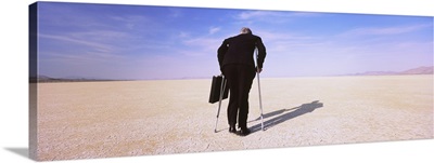 Businessman walking in a desert on crutches with a briefcase, Black Rock Desert, Nevada