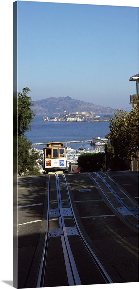 Vertical panoramic photograph of street trolley moving toward the horizon with harbor, waterfront, and mountains in the di...