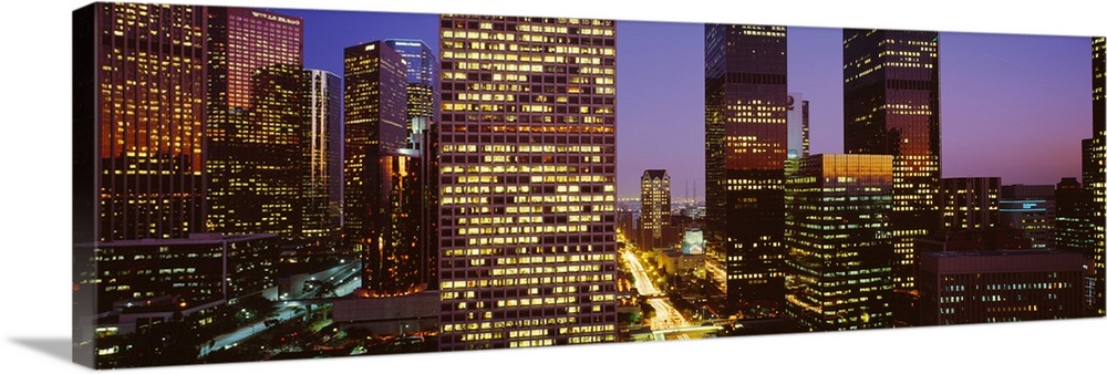 Panoramic, close up photograph of lit skyscrapers at night, in Los Angeles, California, a vivid sky in the background.
