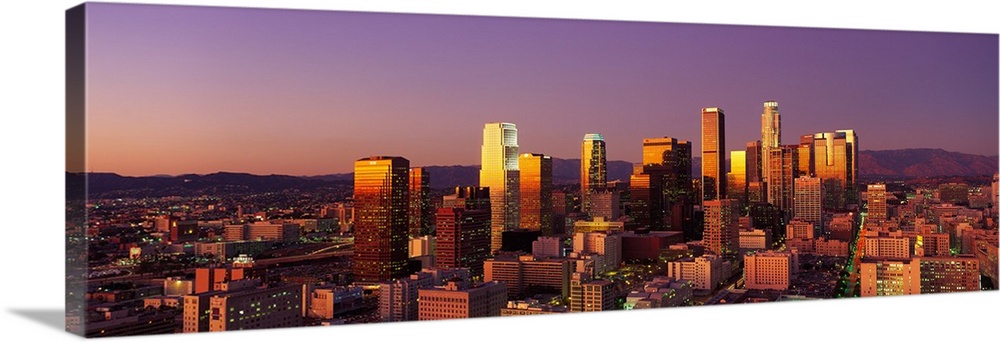 Panoramic photograph of west coast city skyline at dusk.  The buildings and skyscrapers are lit up with a long mountain ra...