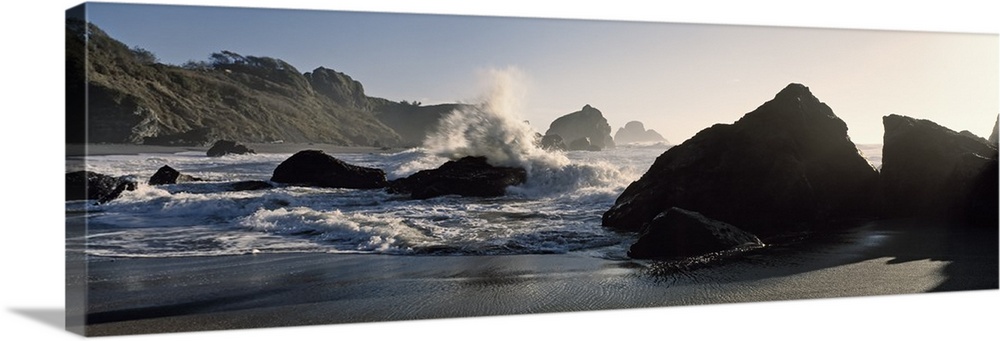 Panoramic photograph of shoreline with huge boulders with ocean waves and spray.
