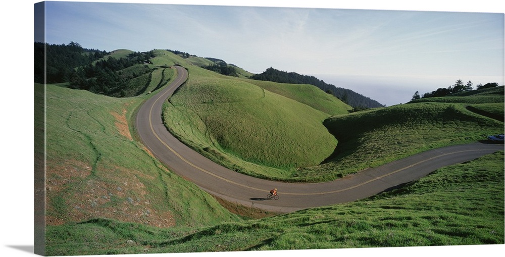 Large, horizontal photograph of a winding road through the green landscape of Bolinas Ridge in Marin County, California.  ...