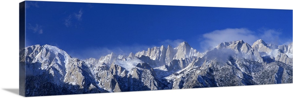 Panoramic photograph of snow covered Mount Whitney beneath a vibrant blue sky in California.