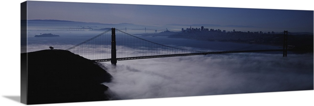 Large panoramic piece of the Golden Gate bridge that has dense fog just under it covering the water below.