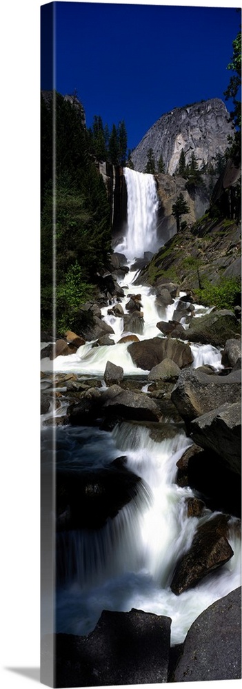 Vertical panoramic photograph of waterfall flowing into a rocky stream surrounded by trees.