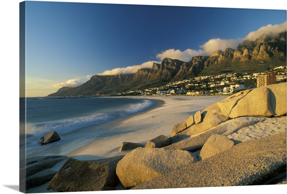 Horizontal, large photograph of rocks on a beach in front of Cape town, South Africa and mountains on the horizon.