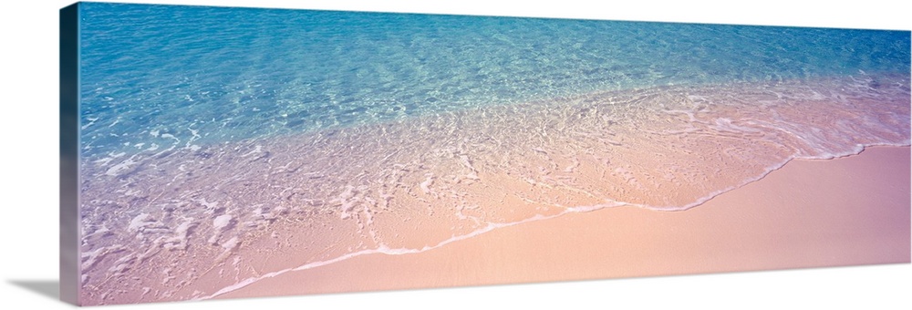 Panoramic photograph concentrates on a small section of clear ocean water as it gently washes onto a sandy shore.