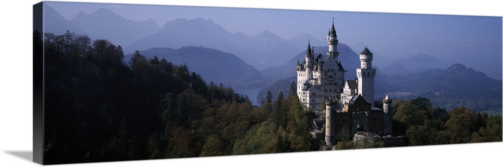A grand historic castle sits perched at the top of a hill in Central Europe, amidst a forest of pine trees and tall mounta...