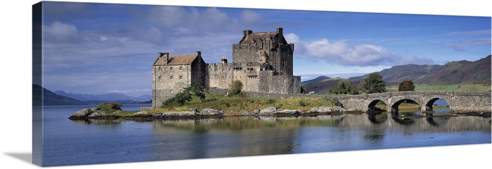 Panoramic photograph of a bridge over Loch Duich, leading to a large, old castle on Eilean Donan Island, mountains in the ...
