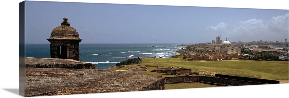 The coast of San Juan is photographed in panoramic view with the ocean to the left and the city on the right.