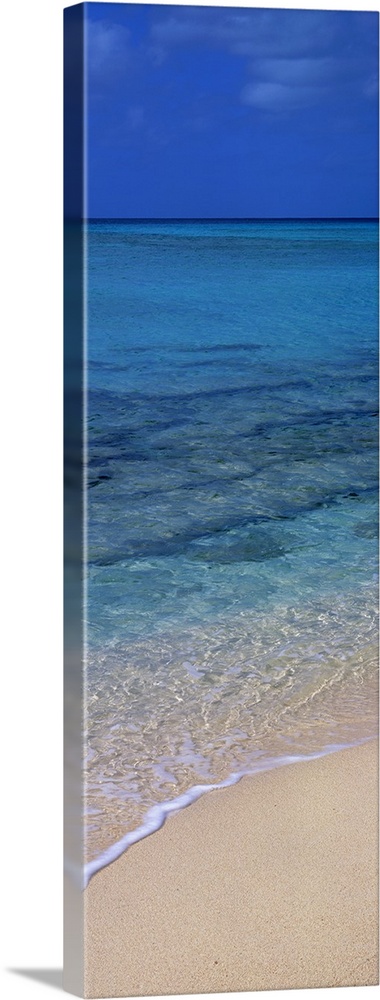 Vertical panorama piece of the crystal clear ocean that is calm as it washes up on the sand.