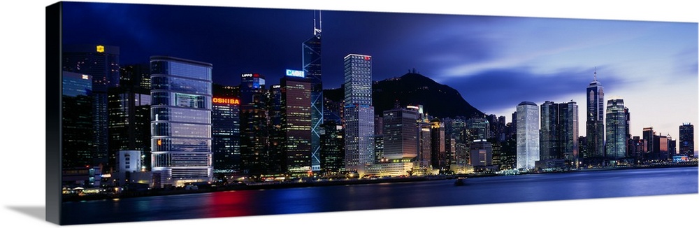 Panoramic photograph displays the bright skyline of a famous city reflecting over a portion of Victoria Harbour.  In the b...