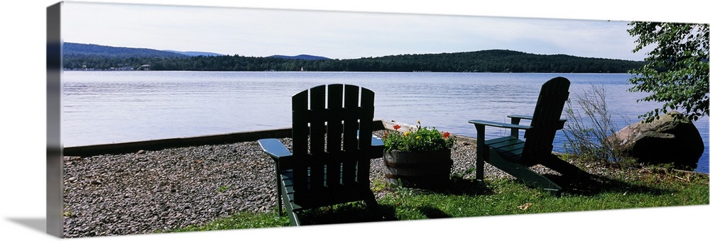A panoramic photograph of Adirondack chairs arranged with a view of a lake on a bright sunny day.