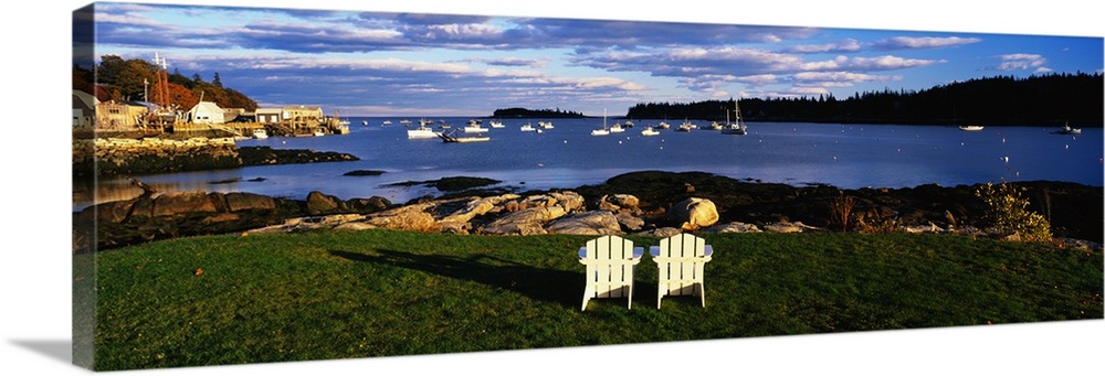 Giant, landscape photograph of two wooden chairs overlooking the coastline onto many boats in blue waters, in Lobster Vill...
