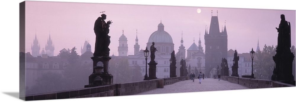 Horizontal photo print of a bridge with people walking across amongst statues and an old town in the distance.