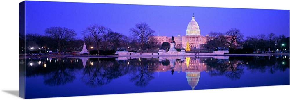 A large panoramic photograph of the US Capitol building lit up during the night. The building and scenery are reflected in...