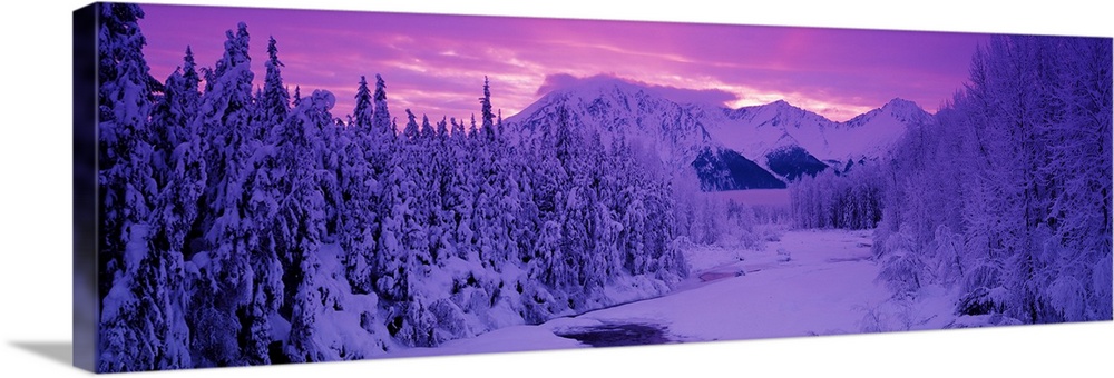 Panoramic photo art of snow covered forests on the left and right of a snowy open space with a sunset in the distance past...