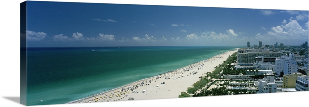 An aerial photograph is taken of the coast in Miami showing a busy beach lined by the teal ocean water.