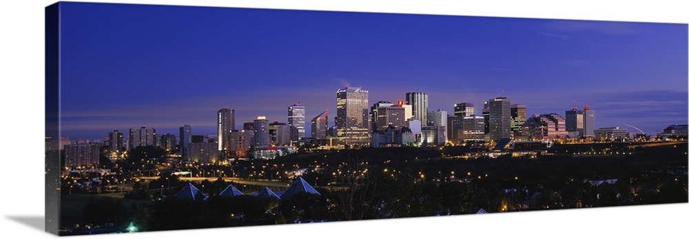 Panoramic photograph of cityscape at dusk with buildings and skyscrapers lit up.