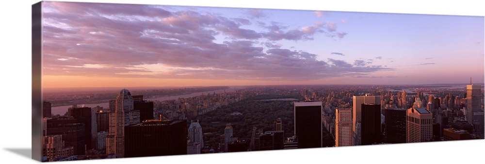 Panoramic photograph of the New York City skyline showing Central Park just behind the buildings in the foreground.