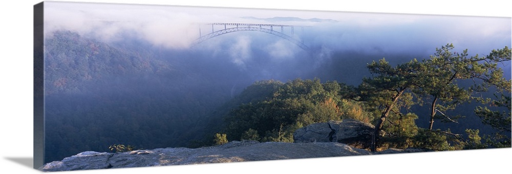 Panoramic image of the new River Gorge Bridge peeking through the fog high above the New River and surrounding Mountains.