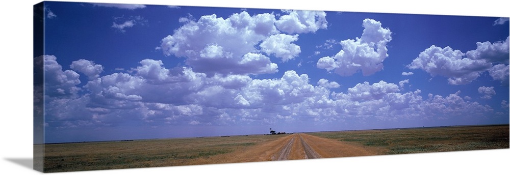 Panoramic photograph taken at the end of a dirt road with flat fields on both sides and large clouds hovering above.