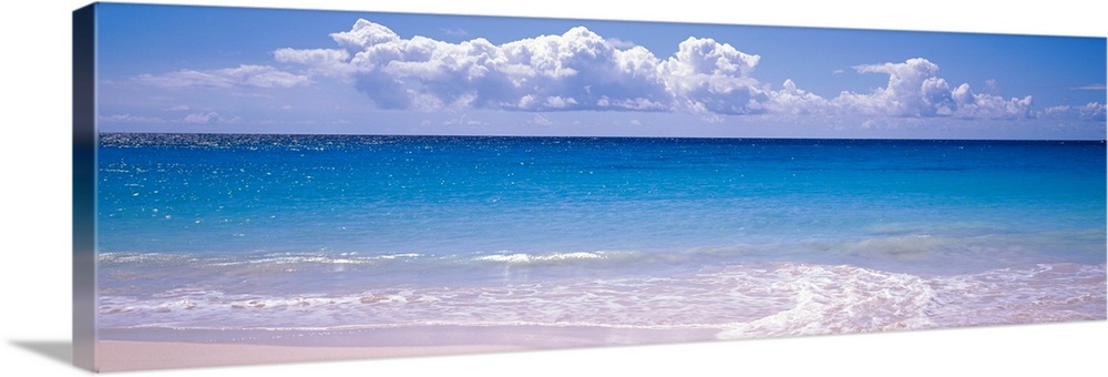 Panoramic photograph shows the sparkly water of an ocean slowly coming into shore on a bright and sunny day.