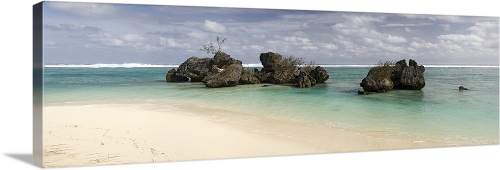 Long horizontal image print of a clear ocean washing ashore past big rocks sticking out of the water.