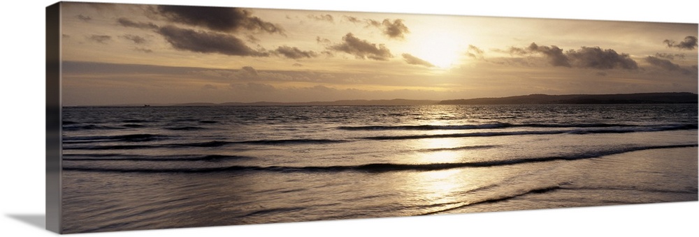 Panoramic photo of the setting sun shining down on the ocean and beach.