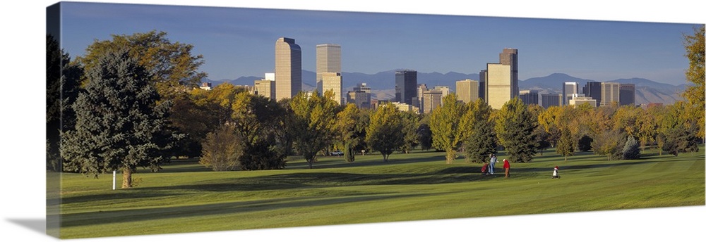 Big, panoramic photograph on the green of a golf course in Colorado, full of trees, the buildings of the Denver skyline in...