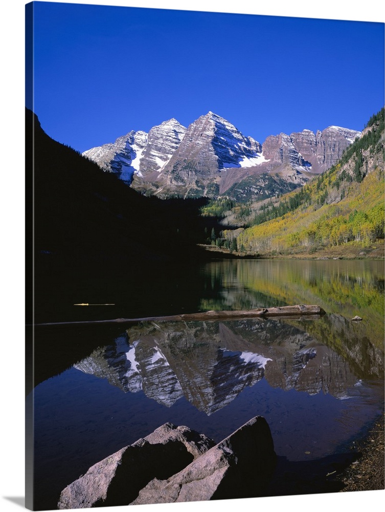 Calm photograph of snowy mountain peaks in the Rocky Mountains, reflected in a still lake of fresh spring water.