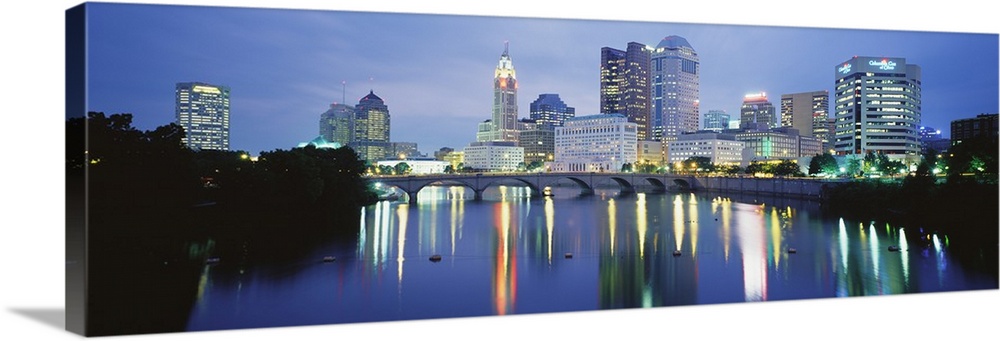 Giant, horizontal photograph of the Columbus skyline at night, reflecting in the waters of the Scioto River, past the Main...