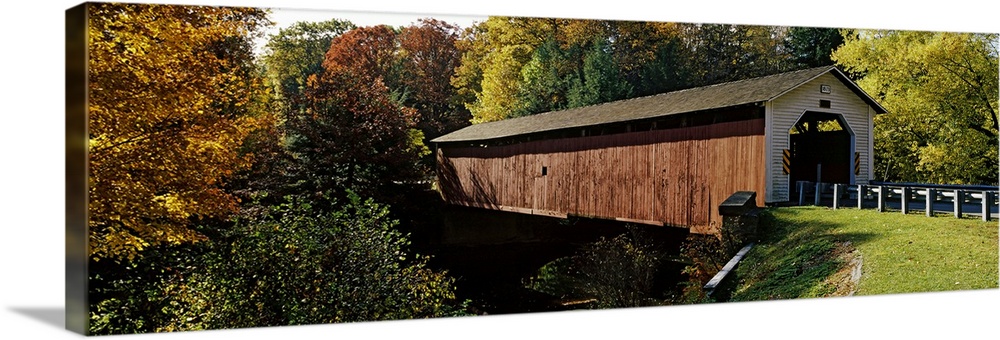 Panoramic photograph of the wooden McGees Mill covered bridge, surrounded by a forest of trees with fall foliage, in Clear...