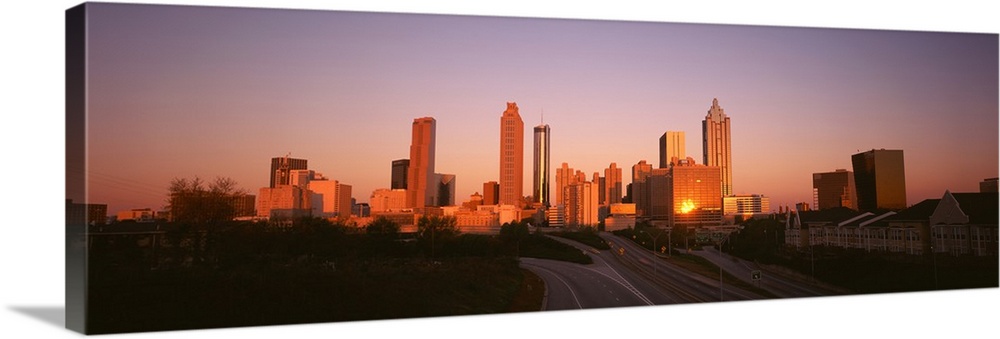 Giant, horizontal photograph of the sun rising over the Atlanta skyline, several roads and a row of buildings can be seen ...
