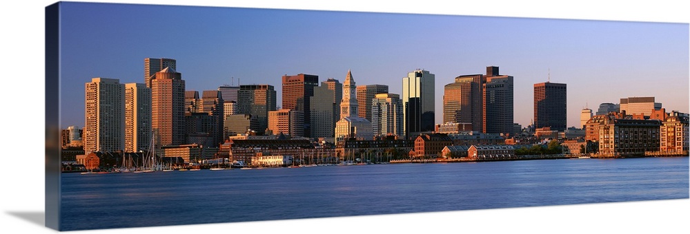 Large panoramic photograph of the Boston skyline from across the river with the sun hitting the buildings as it rises.