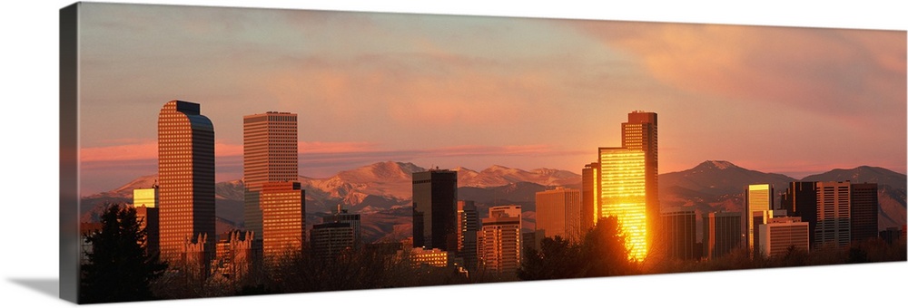 A panoramic shot taken of the Denver skyline while the sun is setting and reflecting off some of the buildings.