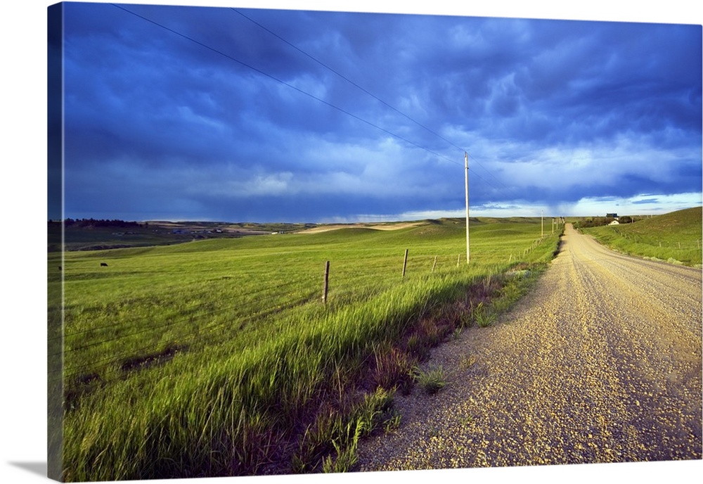 Landscape, oversized photograph of a gravel road, open fields on wither side, beneath a stormy sky of swirling clouds, in ...