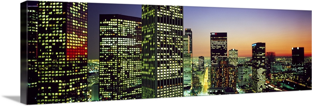 Panoramic photo of an illuminated cityscape up close to the buildings at sunset.