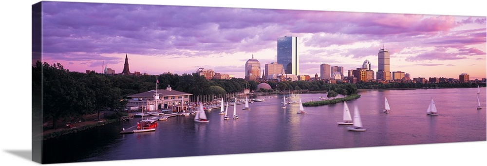 Panoramic photograph of skyline and waterfront at sunset.  There are sailboats in the water under a cloudy sky.