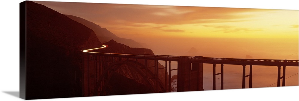 Panoramic photograph of overpass winding through mountains over the ocean at sunset.